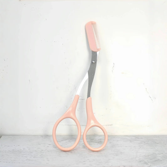 Pink eyebrow trimming scissors with comb on light gray surface